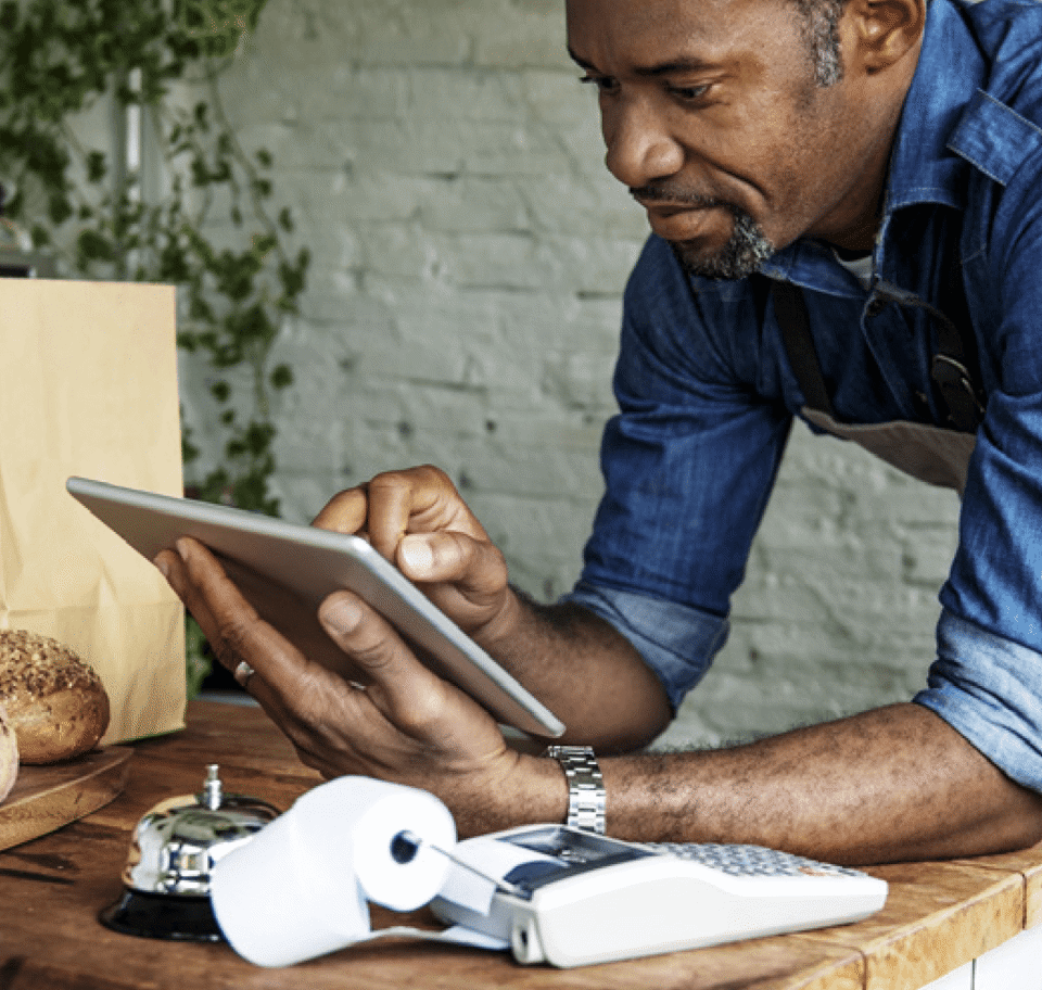 Man at shop counter with bell using tablet